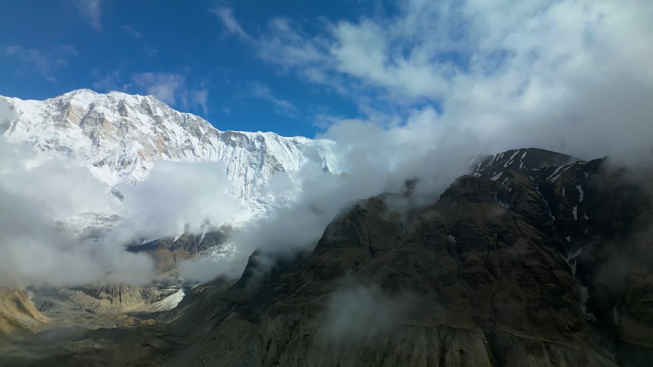 Majestic snow-covered peaks surrounded by drifting clouds near Tilicho Lake in Nepal, showcasing high-altitude mountain beauty with rocky slopes and dramatic Himalayan scenery