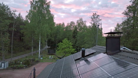 Drone-tilting-over-home-roof-solar-cells,-toward-a-dramatic,-summer-sunset-sky