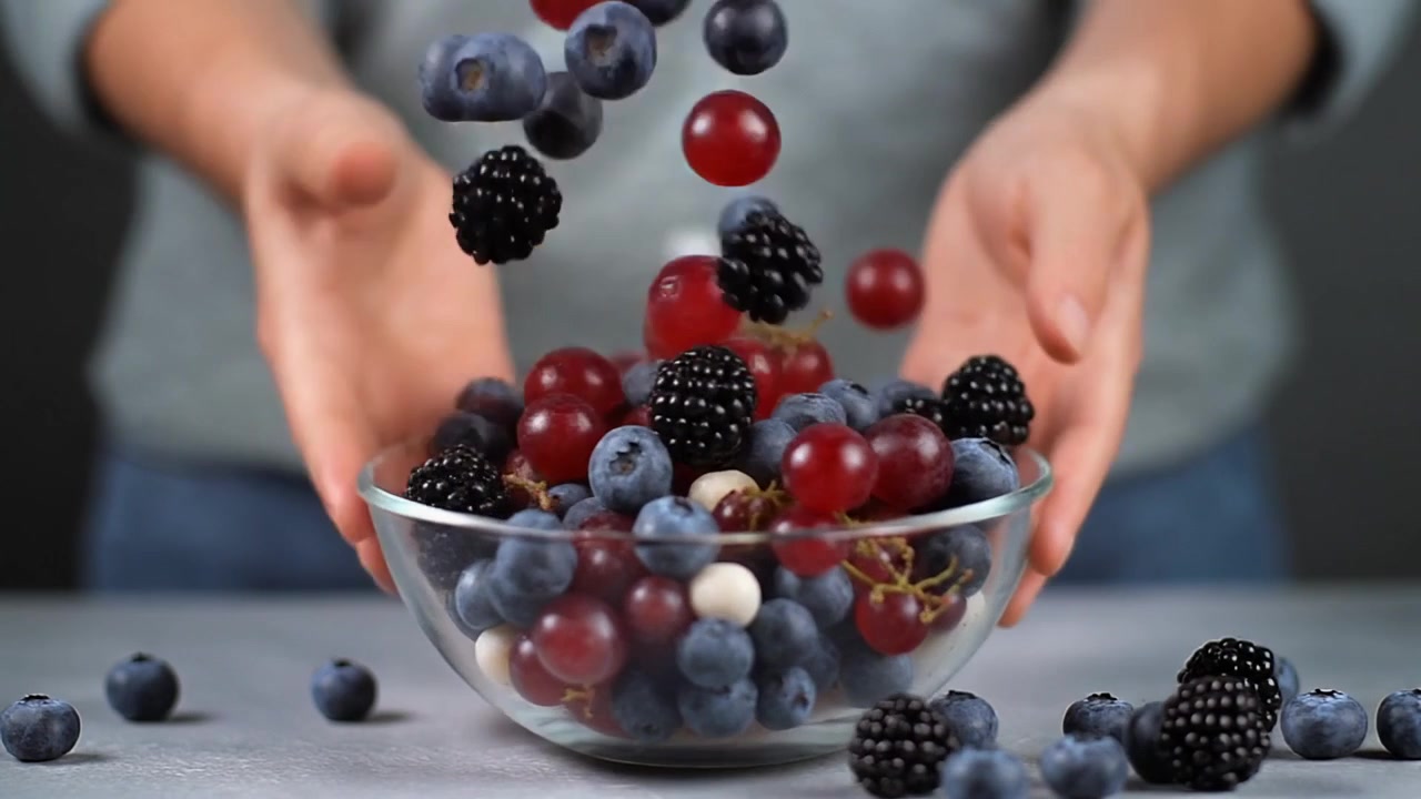Frutti di bosco freschi e uva che cadono in una ciotola di vetro