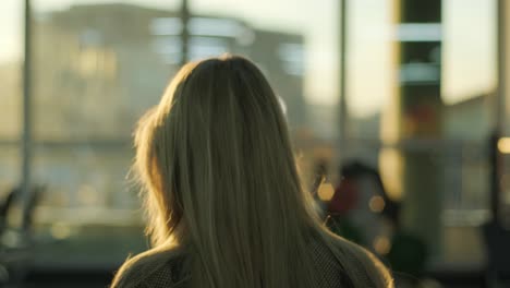 rear view of adorable long-haired blonde woman walking against sunset or dawn background