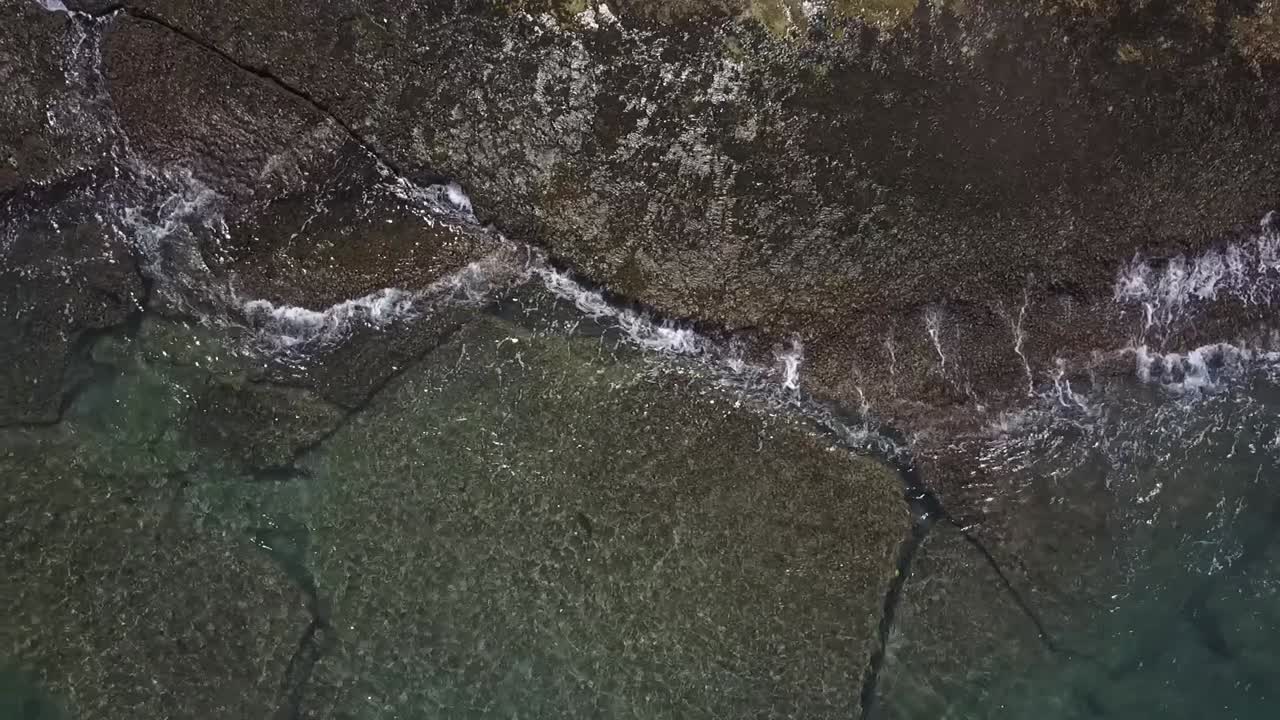 HD drone footage capturing stunning clear ocean water crashing against rugged rocks on the shores of Oahu. Showcasing the power and beauty of Hawaii’s coastline in a breathtaking aerial view.