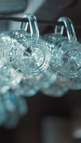 clean glass mugs for beer hang on metal rack in empty pub closeup. shiny glassware prepared for guests serving in bar. public place for alcohol drinking