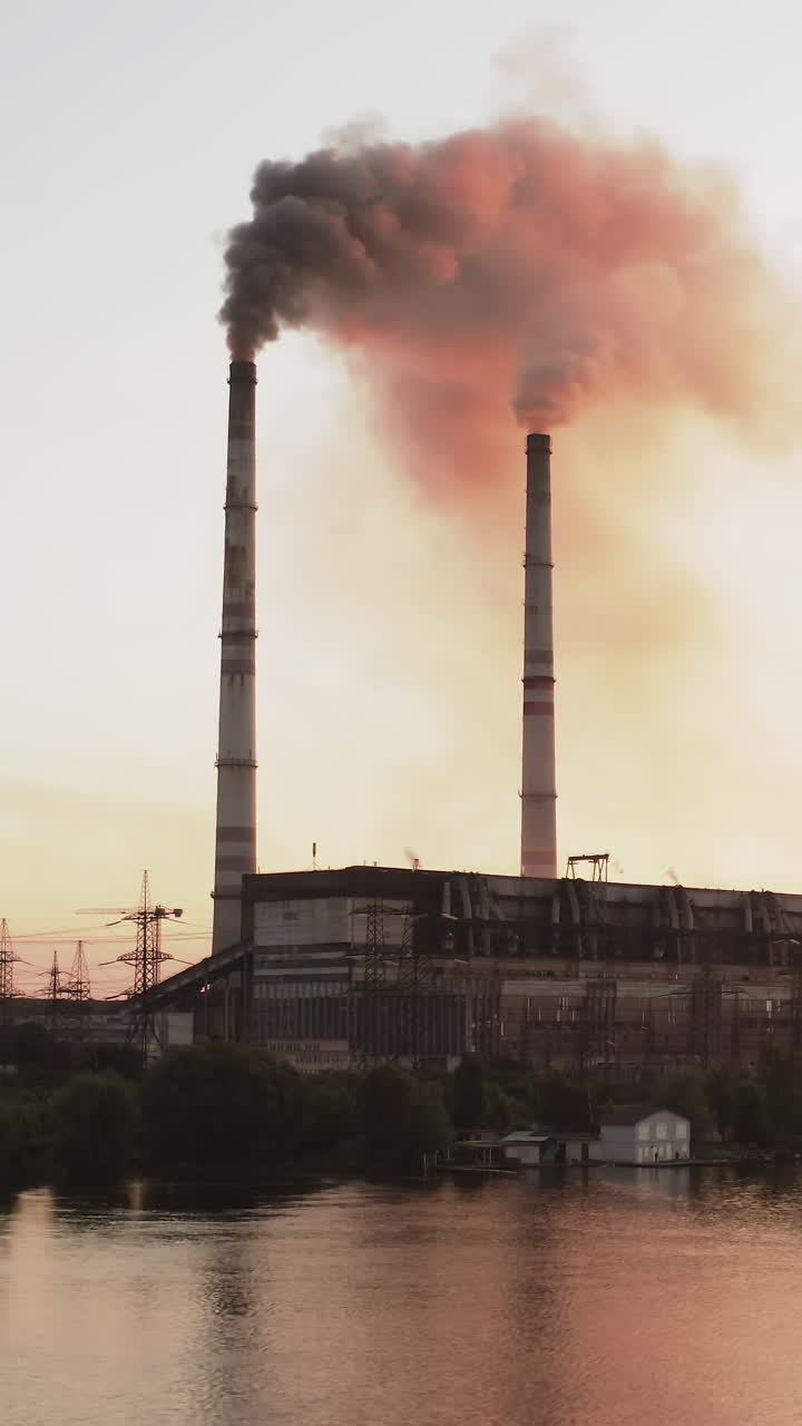 Dark puffs of smoke releases into the atmosphere. Harmful emissions from industrial plant pollute the air near the river at sunset. Ecological disaster. Vertical video