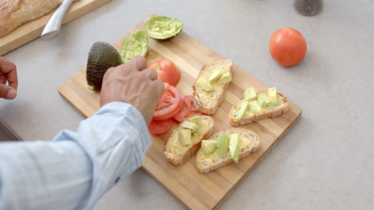 Slicing avocado and arranging on bread slices, man preparing avocado toast in kitchen