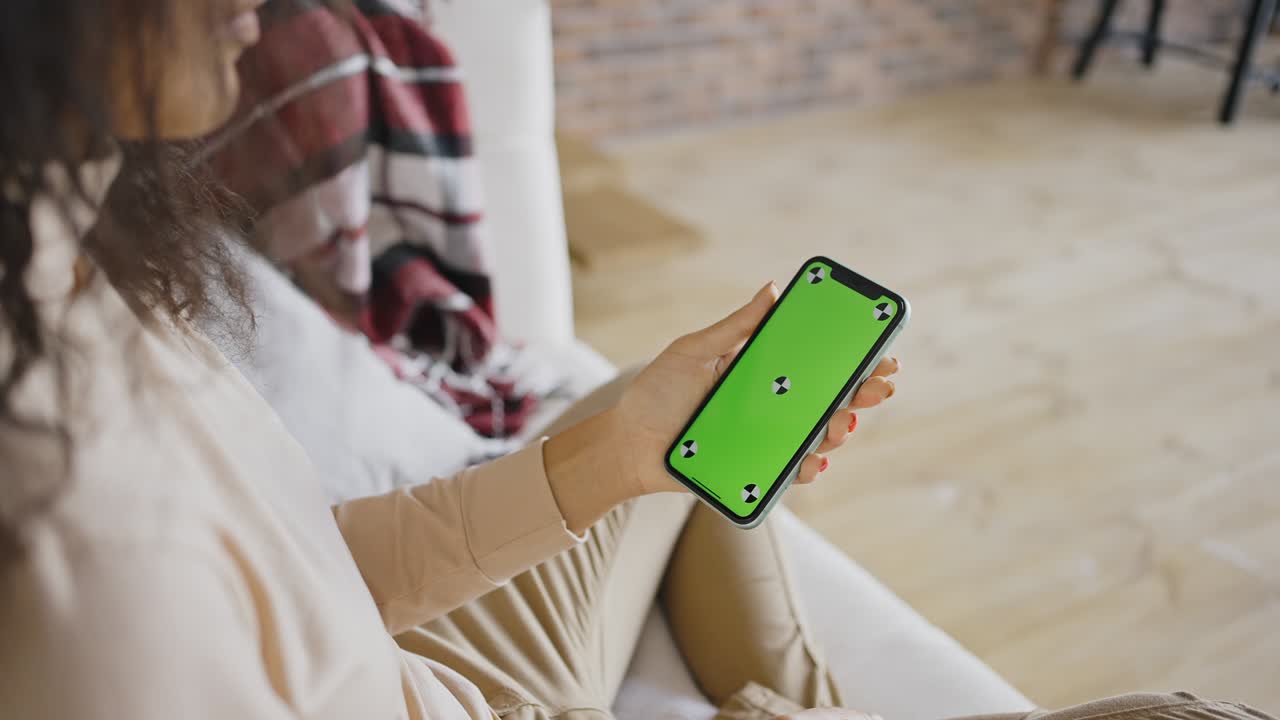 Phone with green screen and chroma key in womans hands. Watching video content close up. Domestic rest and online chat on sofa