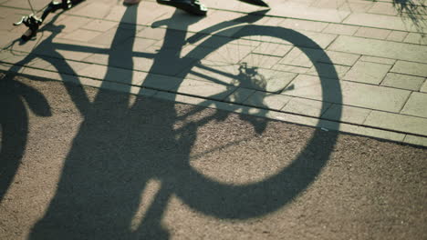 shadow of upside-down bike cast on ground as back tire rotates in motion, creating dynamic silhouette on pavement with warm sunlight filtering through