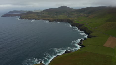 Luftpanoramaaufnahme-Küstenlandschaft.-Wellen,-Die-An-Der-Felsigen-Küste-Zusammenbrechen-Und-Weißen-Schaum-Bilden.-Grüne-Weiden-Und-Dörfer-Auf-Dem-Land.-Irland