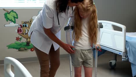 female doctor assisting girl to walk with crutches