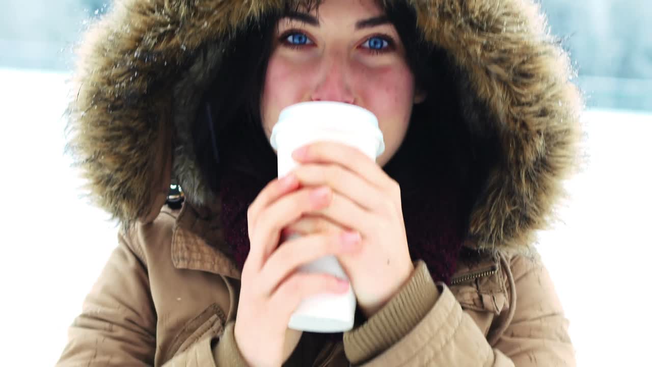 mujer sonriente con chaqueta de piel tomando café durante la nevada