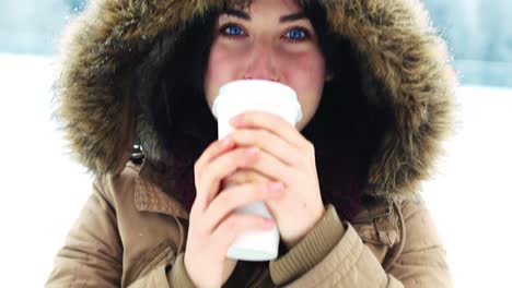 Smiling-woman-in-fur-jacket-having-coffee-during-snowfall