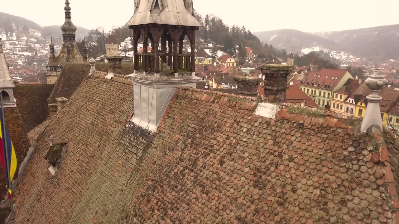 una toma de un dron, capturando la azotea de una arquitectura antigua en la ciudad de sighisoara en una tarde con una bandera comunitaria izada al lado y un paisaje urbano en el fondo