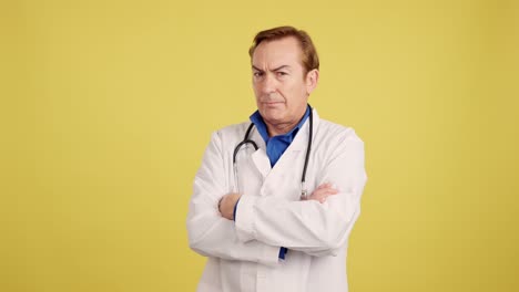 serious male doctor with arms crossed against a yellow background