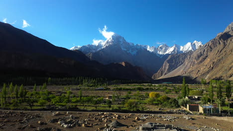 cinematic drone shot of the sun shining in the valley, passu cones in hunza pakistan, snow covered mountain peaks with steep cliffs, moving towards mountains from low level