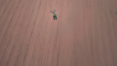 high aerial drone view of tractor flattening field with rollers, monoculture