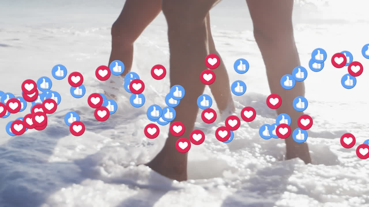 Icone a forma di cuore e "mi piace" che fluttuano, con la parte inferiore di una coppia che cammina nell'acqua sulla spiaggia.