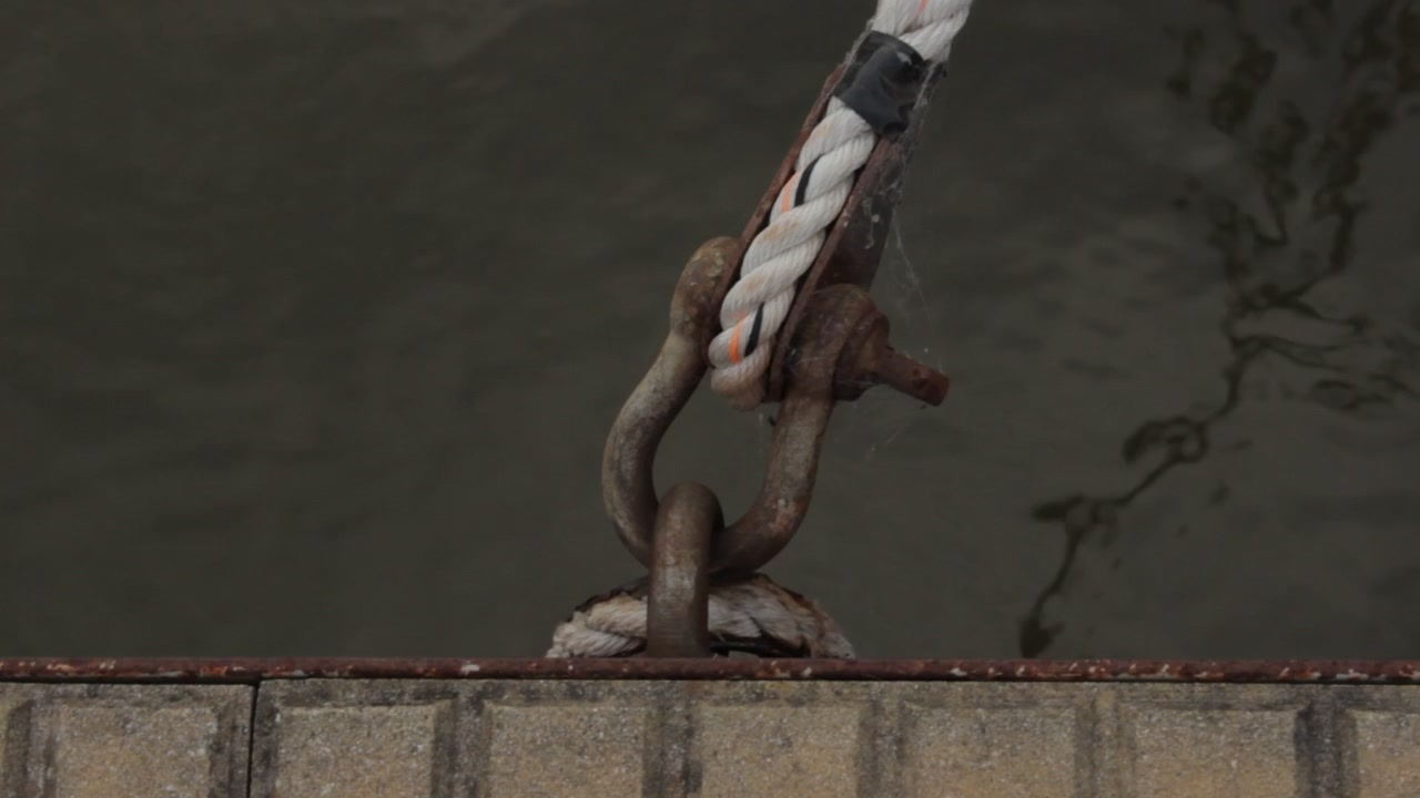 Close up of a rusty nautical shackle anchored to the marina dock, to keeping the sailboats for drifting away in the water, with a white rope