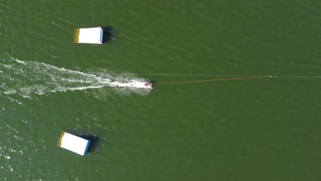 birds eye view drone shot of a waterski system - drone is ascending over some ramps with waterskiers and wakeboarders passing by