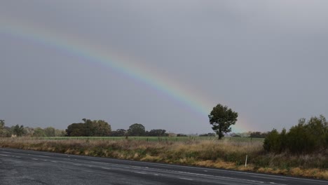 rainbow gradually fades in a cloudy rural setting