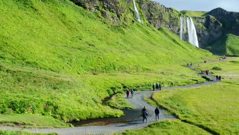 tourists walking on a path between seljalandsfoss and gljufrabui waterfalls on a sunny day in iceland