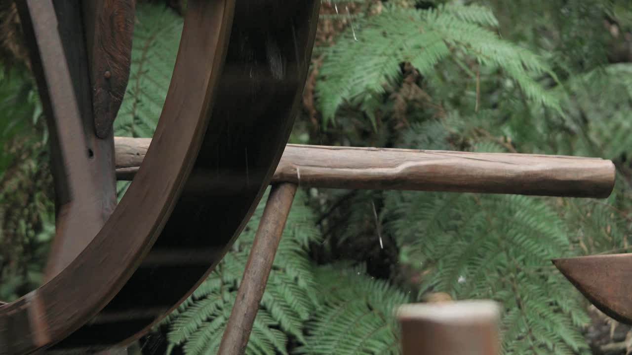 Close up view of the lower section and wooden structure of a traditional water wheel turning continuously in a lush green environment