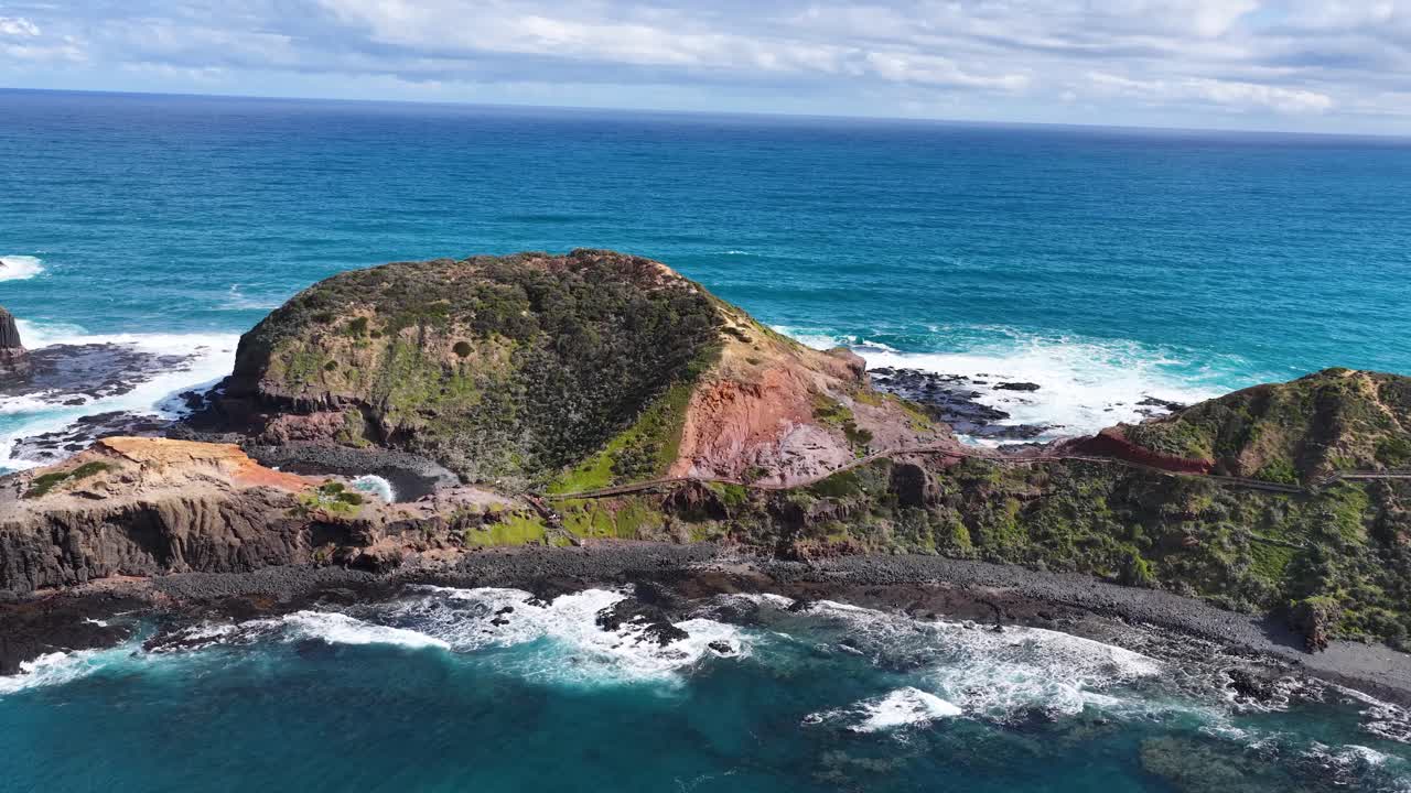 Drone glides toward dramatic rocky coastline, turquoise ocean, and lush cliffs under daylight skies