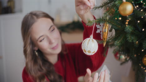 happy beautiful woman hanging bauble on christmas tree at home