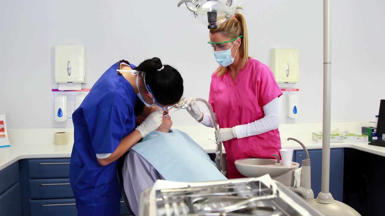 Dentista examinando los dientes de un paciente con un asistente