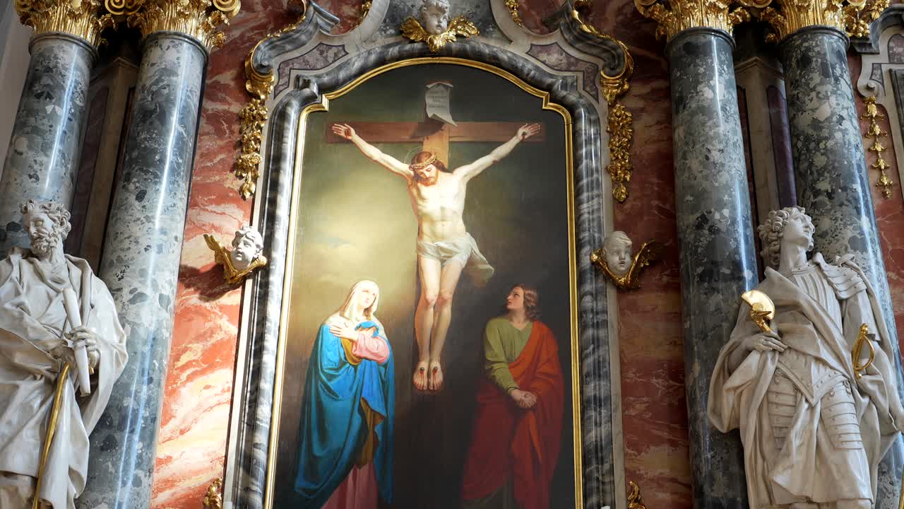 Záběry velkého náboženského olejového obrazu zobrazujícího Ježíše na kříži obklopeného barokní architekturou