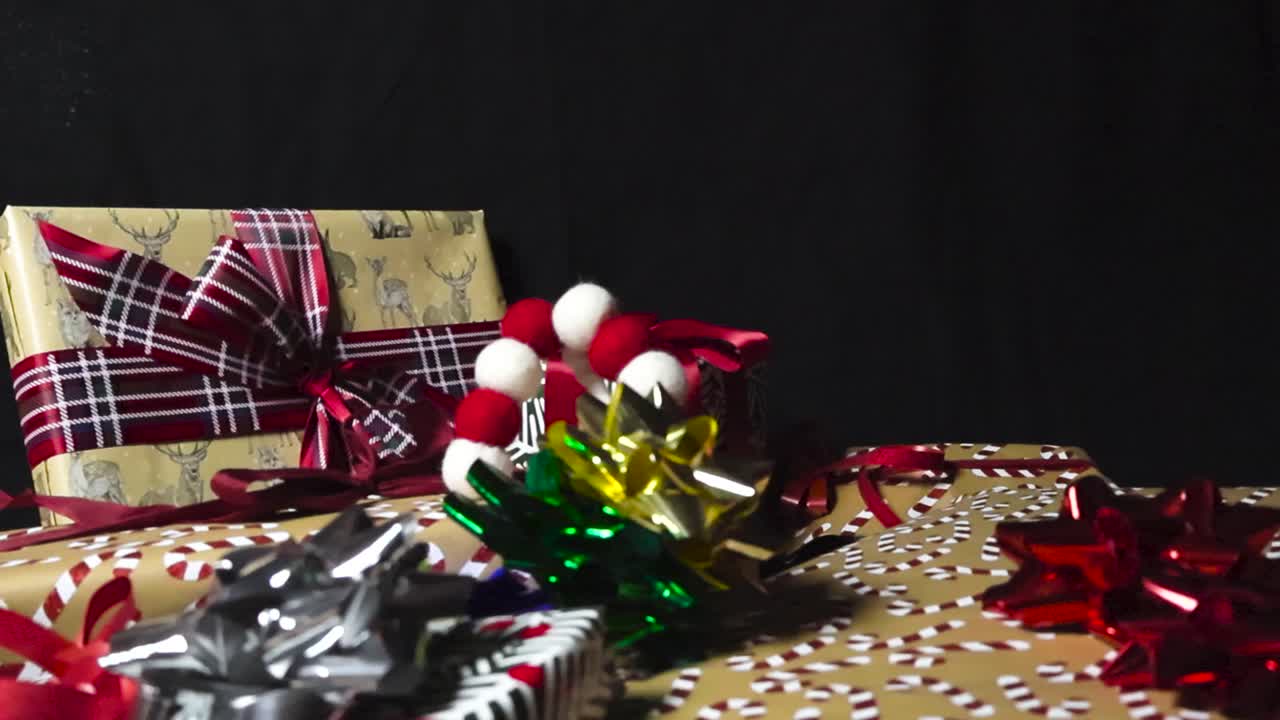imágenes de cerca o de cerca de regalos y regalos en papel de envolver colorido y hermoso y cintas sobre un fondo negro mientras que las cintas de navidad y las decoraciones de roseta caen sobre ellos en cámara lenta