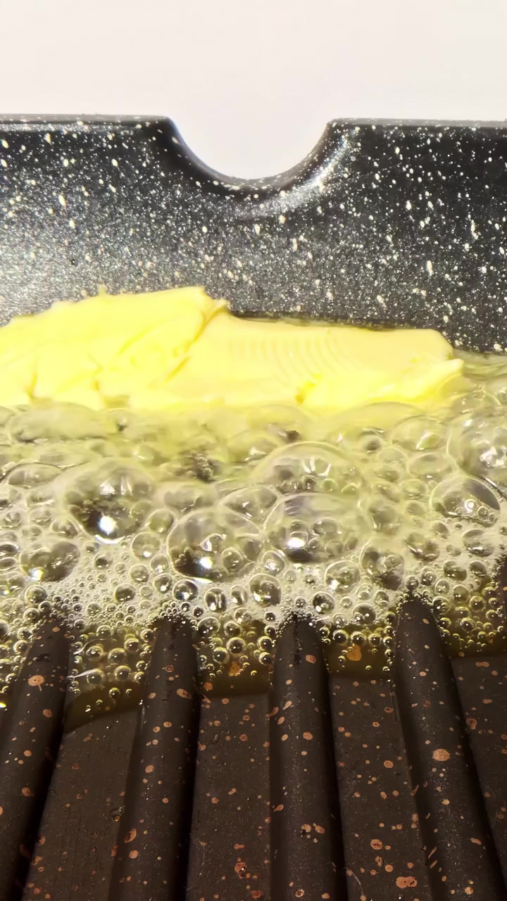 Butter gently melts and bubbles on a black speckled grill pan, creating a warm and inviting cooking scene.