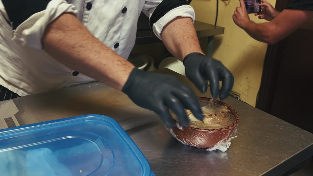 Gloved hands unwrap plastic film from a patterned bowl filled with shredded meat and onions on a metal surface in Miami