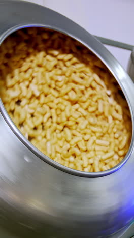 two metal tanks full of sweet snacks rotating and mixing. tasty snack product manufacturing at modern plant. vertical video