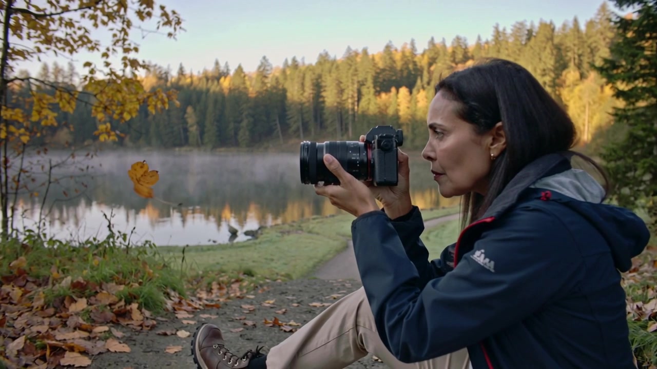 Adjusting camera as drifting leaf prompts woman in blue jacket shooting shore with DSLR, copy space