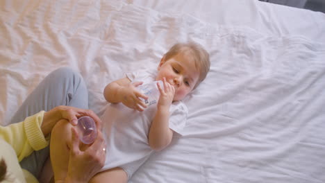 top view of a baby lying on the bed in the bedroom while drinking water from feeding bottle