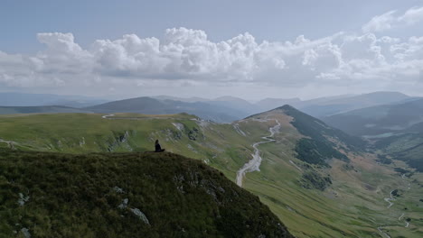 lone individual overlooking vast green landscapes of the transalpina in romania, with dramatic cloudscape and distant rolling hills