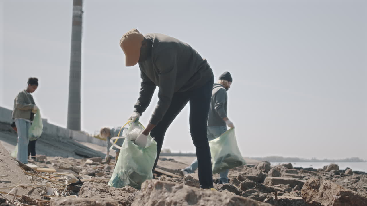 Black Man Collecting Garbage on Shore with Environmental Activists