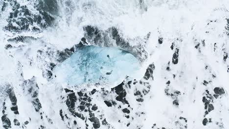 Atemberaubende-Drohnenaufnahme-Von-Wellen,-Die-Auf-Einem-Wunderschönen-Eisfelsen-Am-Diamond-Beach-In-Island-Brechen