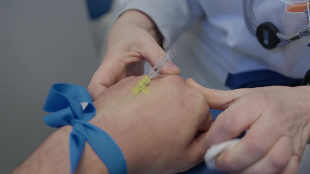 Mani dell'infermiera inseriscono una cannula nel braccio di un paziente con un laccio emostatico blu legato sopra il gomito.