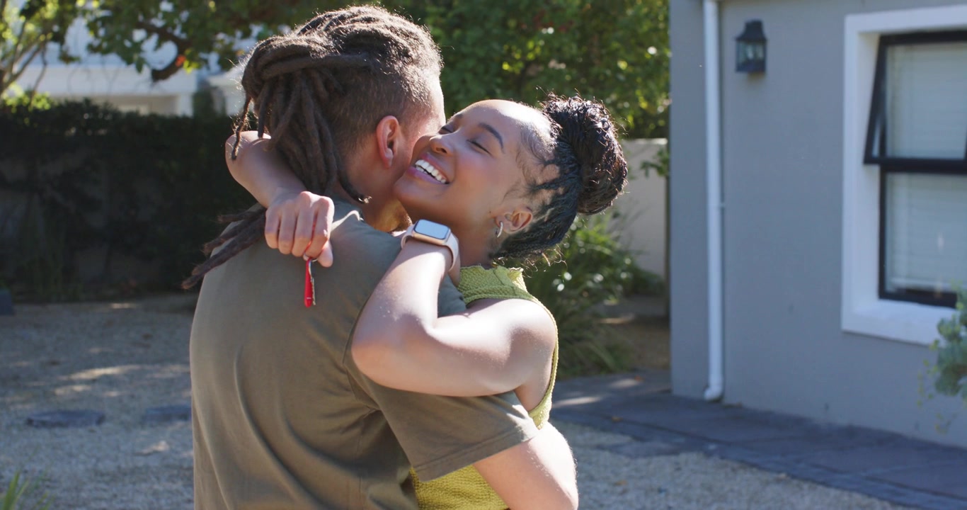 Couple embracing on driveway, woman in green top holding red key fob, reuniting after arriving home