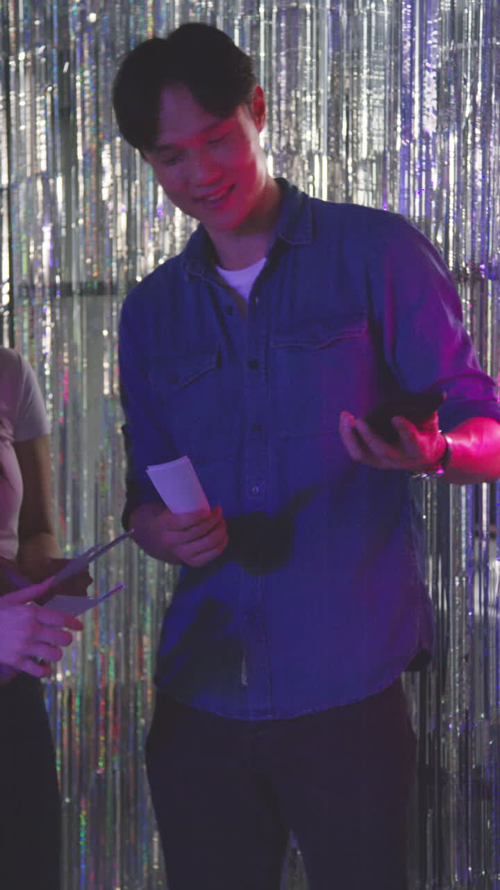 video vertical de un grupo de amigos tomando selfies divirtiéndose mirando las impresiones de la cabina de fotos en un club nocturno o feria 2