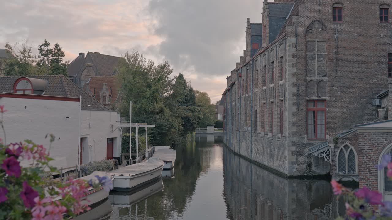 An atmospheric view at dusk in Bruges, Belgium, capturing a tranquil canal flanked by the imposing Gothic brick architecture of the Sint-Janshospitaal (Old St. John's Hospital)