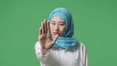 close up of asian muslim woman disapproving with no hand sign while standing in the green screen background studio