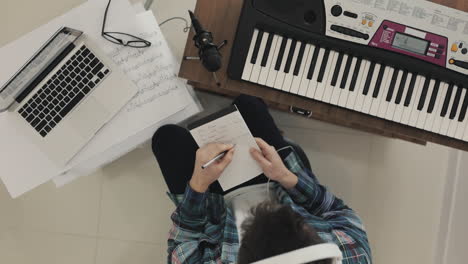 joven músico masculino creando música, descartando ideas y tomando notas en casa