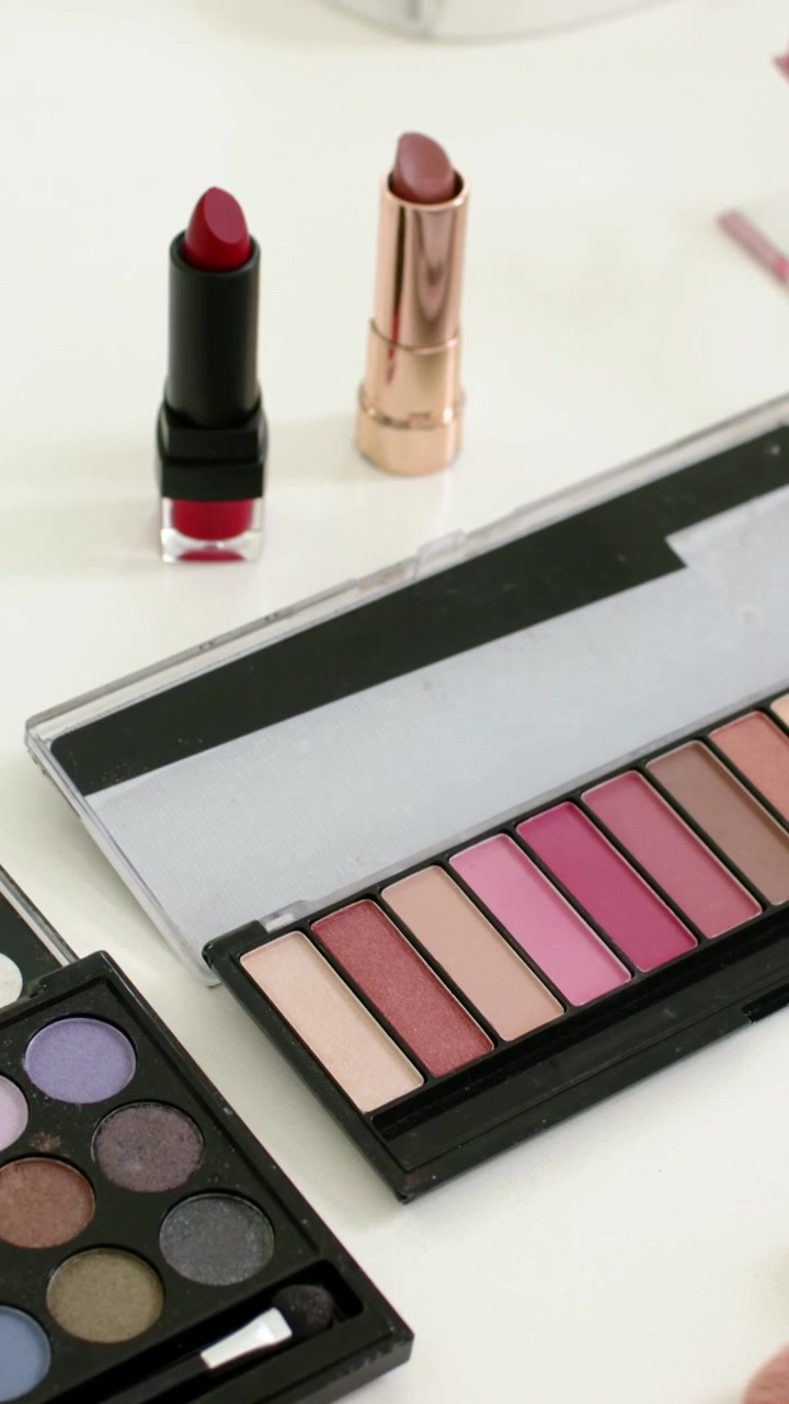 Vertical video: Zooming camera on white table displaying two lipsticks and pink and dark palettes