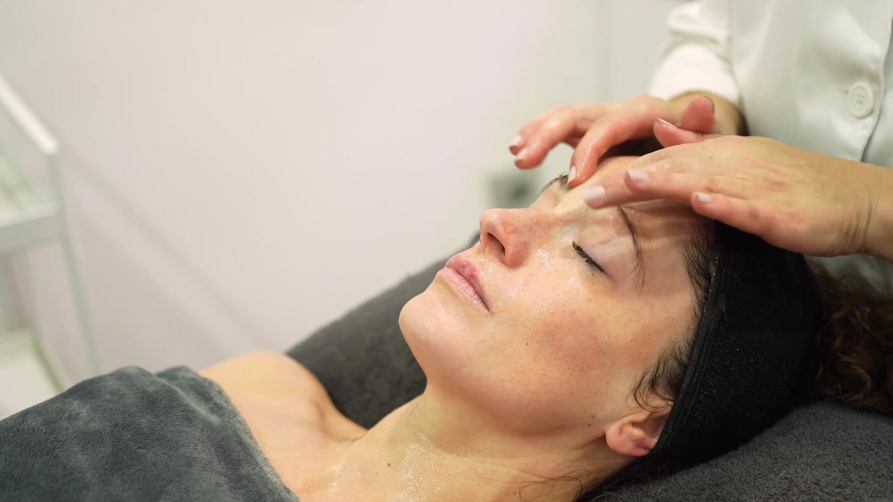 Kosmetikerin massiert Kundin im Gesicht mit kosmetischer Maske im Schönheitssalon.