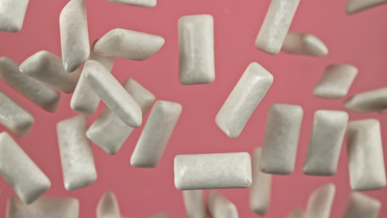 Pezzi di gomma da masticare bianca che cadono in super slow motion su sfondo rosa