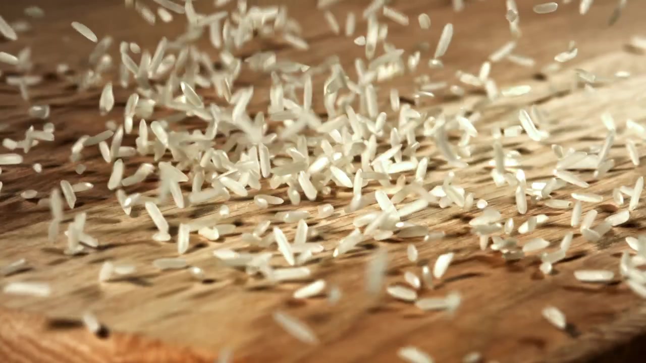 Chicchi di riso bianco che cadono al rallentatore su una superficie di legno