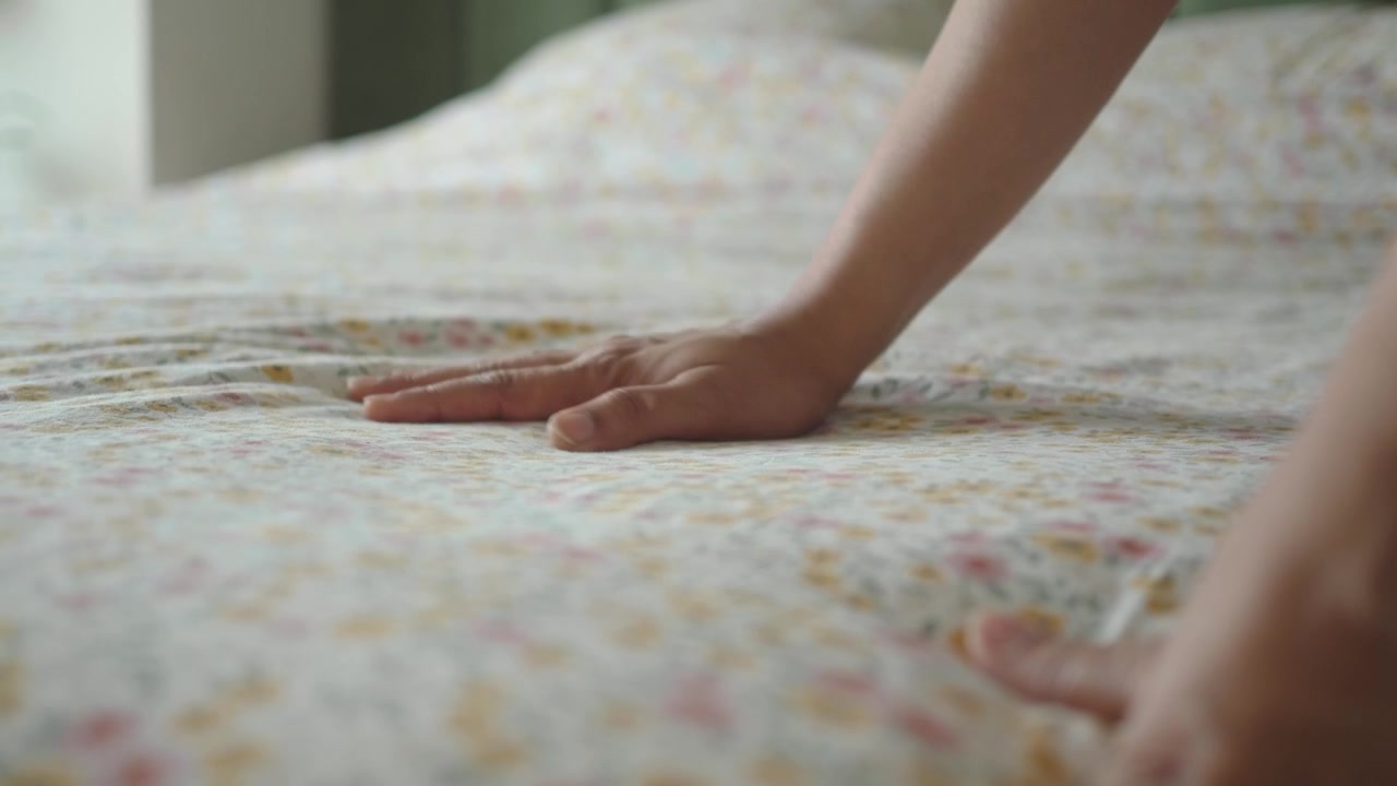 Person Smoothing Floral Bed Sheets on a Bed