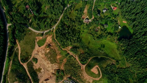 Top-down-drone-view-of-lush-green-forest-wilderness-town-with-lakes,-houses-and-roads-in-between