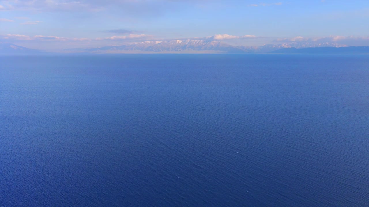 Paesaggio aereo del Lago Sayram a Yili, Xinjiang, con le montagne innevate del Tianshan. Yacht che naviga su un lago alpino circondato da una foresta di conifere e praterie. Paesaggio naturale del Lago Sayram nella Cina nord-occidentale.